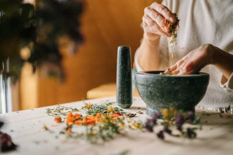 Hands preparing dried, calming herbs in a stone mortar and pestle to make natural remedies for mental health