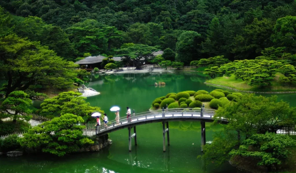Tranquil Japanese healing garden with arched bridge over emerald pond, surrounded by lush greenery and manicured shrubs, exemplifying nature therapy landscape design